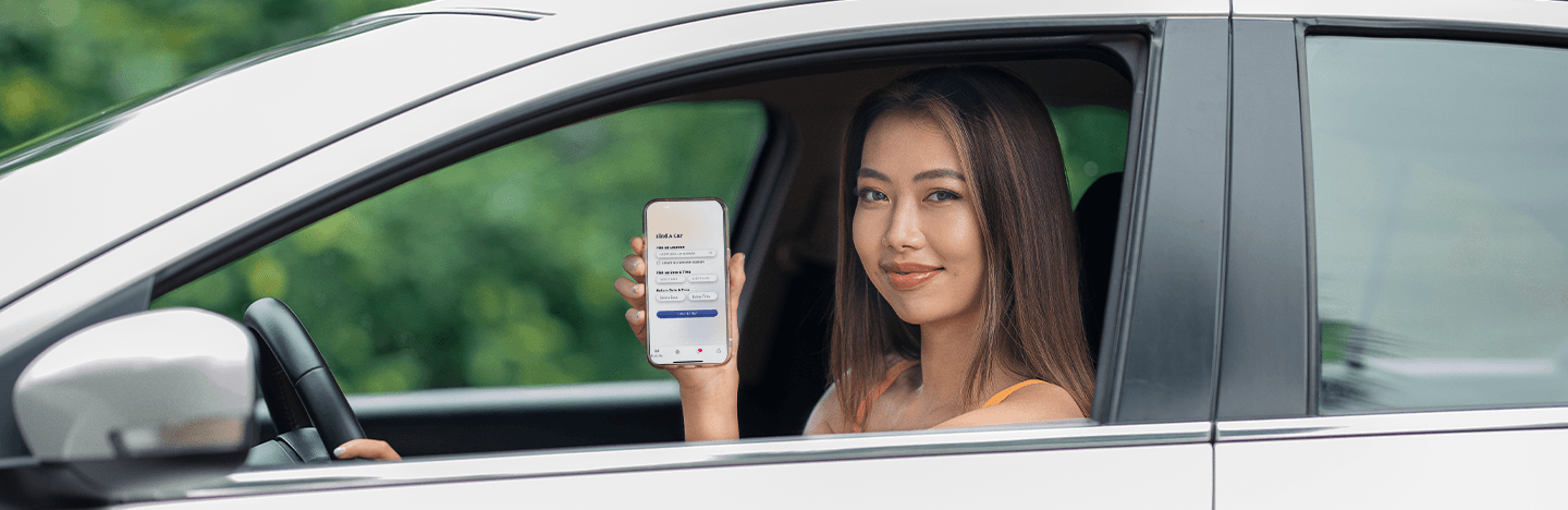Member Benefits Happy woman sitting in a car and showing Yoma Car Share 2.0 app on mobile phone